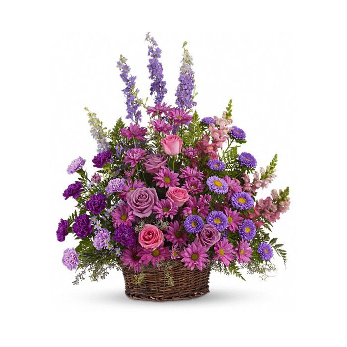 Purple, pink and lavender petals abound in a lovely mix of flowers such as roses, carnations, snapdragons, larkspur, matsumoto and monte cassino asters, nestled among leatherleaf fern and eucalyptus in a round wicker basket.